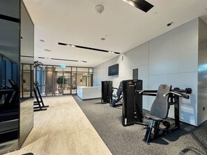 Ein modernes Fitnessstudio mit Trainingsgeräten, einer Rezeption und einem Glastür-Eingang.