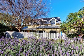 Uma casa com cerca branca, rodeada por campos de lavanda.