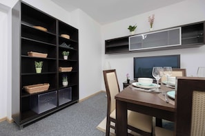 Un comedor con una mesa dispuesta para dos, un mueble bajo con cestas y plantas, y un televisor montado sobre la mesa.