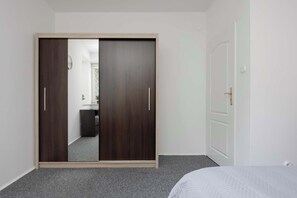 Ein Schlafzimmer mit Kleiderschrank, Bett und angrenzendem Badezimmer, durch eine offene Tür sichtbar.