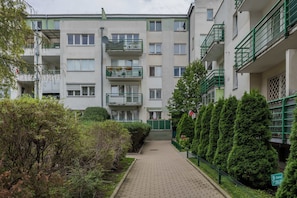 Un edificio residencial de varios pisos con balcones, un sendero empedrado y vegetación.