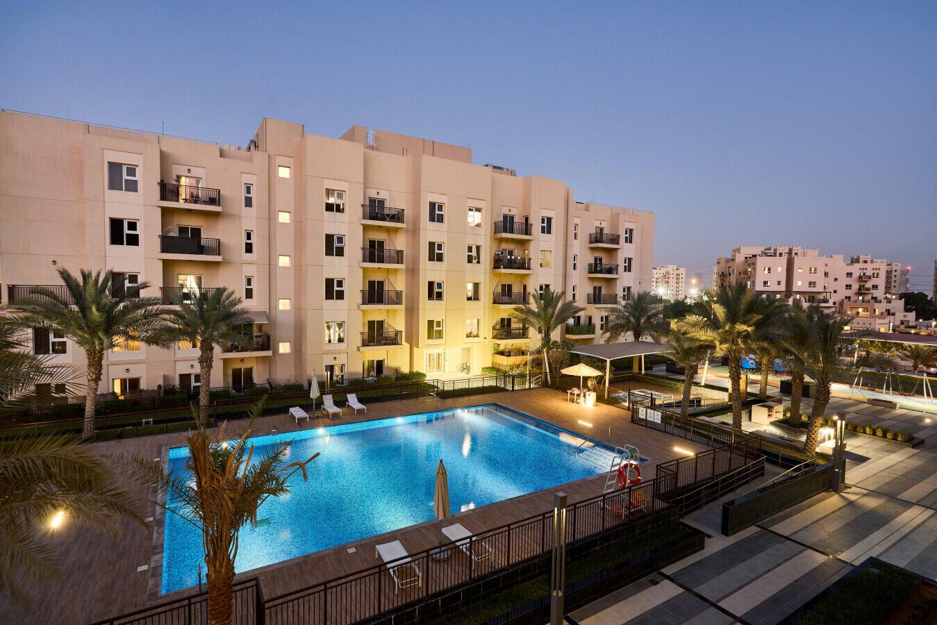 A hotel with a swimming pool, palm trees, and a well-lit balcony area.