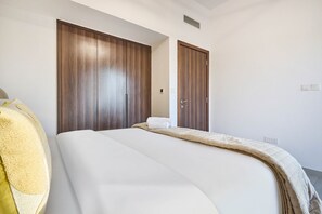 A hotel room with a bed, a wooden wardrobe, and a door. - Family-Friendly 2BR in Remraam with Pool View (Dubai)