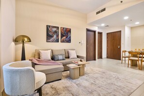 A modern living room with a sofa, coffee table, and a pet bed. There are two doors leading to other rooms. - Family-Friendly 2BR in Remraam with Pool View (Dubai)