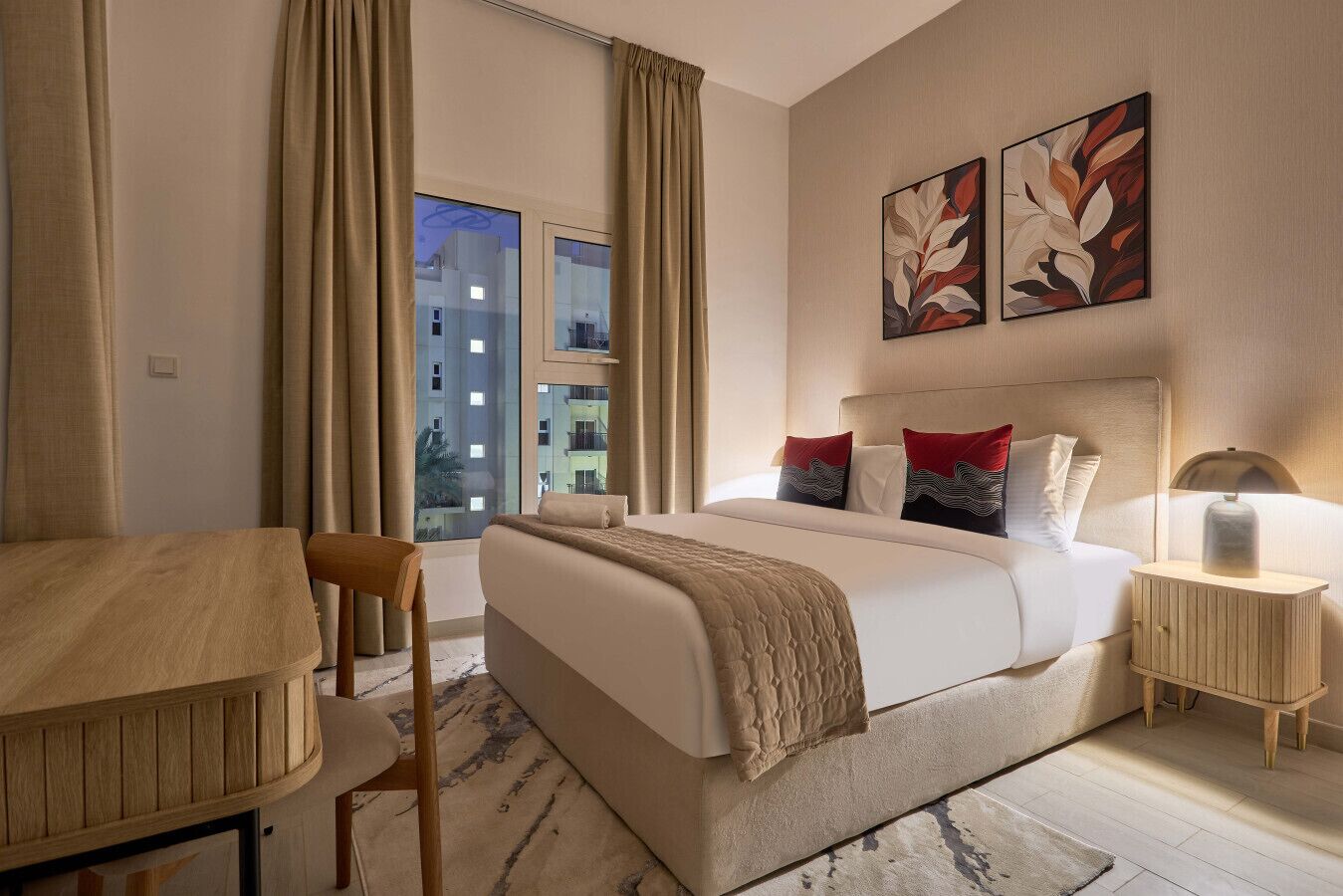 A hotel room with a bed, a desk, a chair, a nightstand, and artwork on the wall.