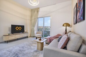 A modern living room with a flat-screen TV, a sofa, a coffee table, and a balcony with a view. - Family-Friendly 2BR in Remraam with Pool View (Dubai)