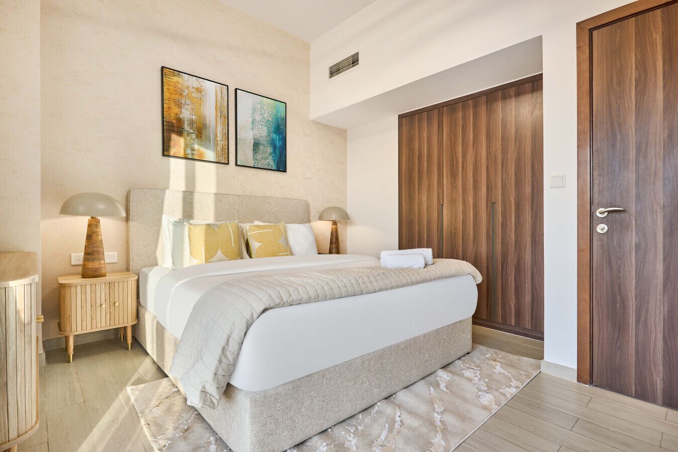 Une chambre avec un grand lit, une armoire en bois et deux tableaux accrochés au mur.