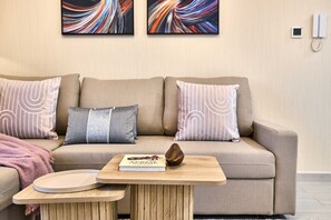 A living room with a sofa, two pillows, a small wooden table, and a book. - Family-Friendly 2BR in Remraam with Pool View (Dubai)