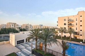 A residential building with a rooftop pool, palm trees, and a view of other buildings. - Family-Friendly 2BR in Remraam with Pool View (Dubai)