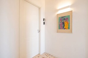 Ein Flur mit einer weißen Tür, einem gerahmten Kunstwerk an der Wand und einer Leuchte darüber.