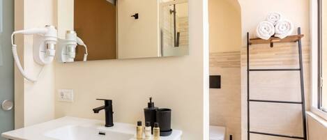 A bathroom with a white sink, black faucet, and a mirror above it. There are toiletries on the sink and a towel rack with towels.