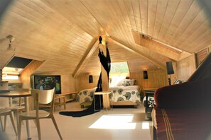 Ein gemütliches Schlafzimmer im Dachgeschoss mit schrägen Wänden, einem Bett mit gemusterten Betttextilien, einem kleinen Tisch, einem Stuhl und einem Fernseher.
