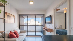 Un soggiorno moderno con un divano, cuscini rossi, una TV e un balcone con vista sulla città.