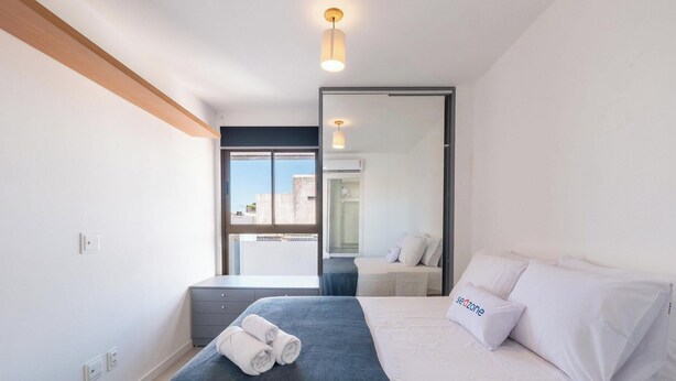 Una camera da letto moderna con un letto, un comodino, una finestra e una lampada a soffitto.