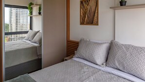 A bedroom with a large window, a bed with patterned bedding, a small bedside table, and a wall-mounted plant. - Ap With Pool, 350 m From Barra Beach Blb1502 (Salvador)