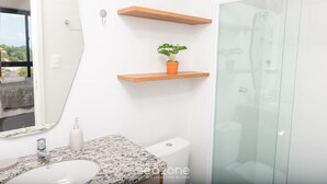 A bathroom with a white sink, a toilet, and a glass shower enclosure. There are wooden shelves above the sink and a potted plant on one of the shelves. - Ap With Pool, 350 m From Barra Beach Blb1502 (Salvador)