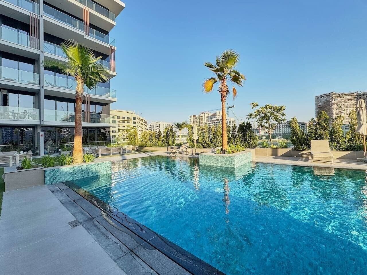 Una piscina con acqua cristallina e blu, circondata da palme e edifici moderni.