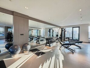 A gym with exercise equipment, large windows, and a modern interior design. - Chic Studio | Pool View Balcony | Avelon Arjan (Dubai)