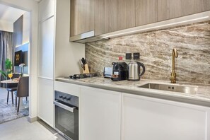 A modern kitchen with a marble backsplash, stainless steel appliances, and a gold faucet. - Chic Studio | Pool View Balcony | Avelon Arjan (Dubai)