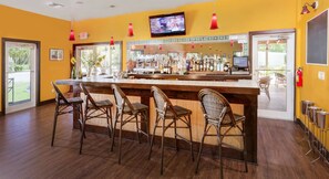 Eine Bar mit Korbstühlen, einer Theke mit Flaschen und einem an der Wand montierten Fernseher.