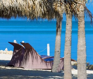 Ein Strand mit einer Struktur aus Reet, Palmen und einem klaren, blauen Meer.