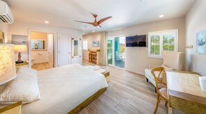Ein Hotelzimmer mit Bett, Schreibtisch, Sessel, Deckenventilator, Fernseher und einem Balkon mit Aussicht.