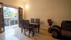 Un comedor con una mesa y sillas, un sofá, una planta en maceta y vistas al exterior a través de un ventanal.