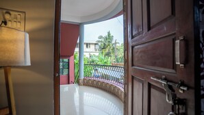 Puerta abierta que da a un balcón con suelo de baldosas, baranda de metal y vista a un edificio con una palmera.