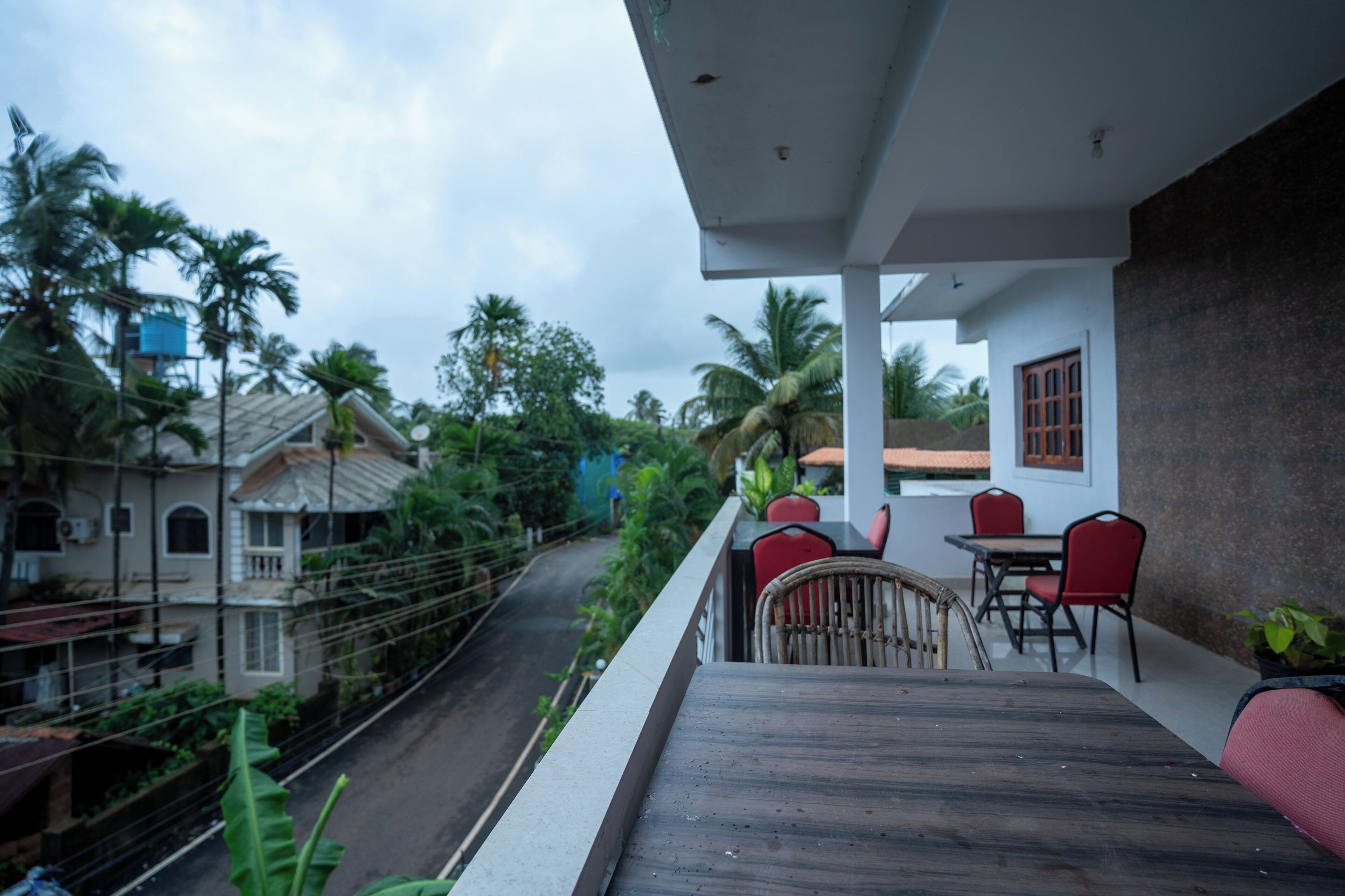 A balcony with a table and chairs, overlooking a street with houses and palm trees.