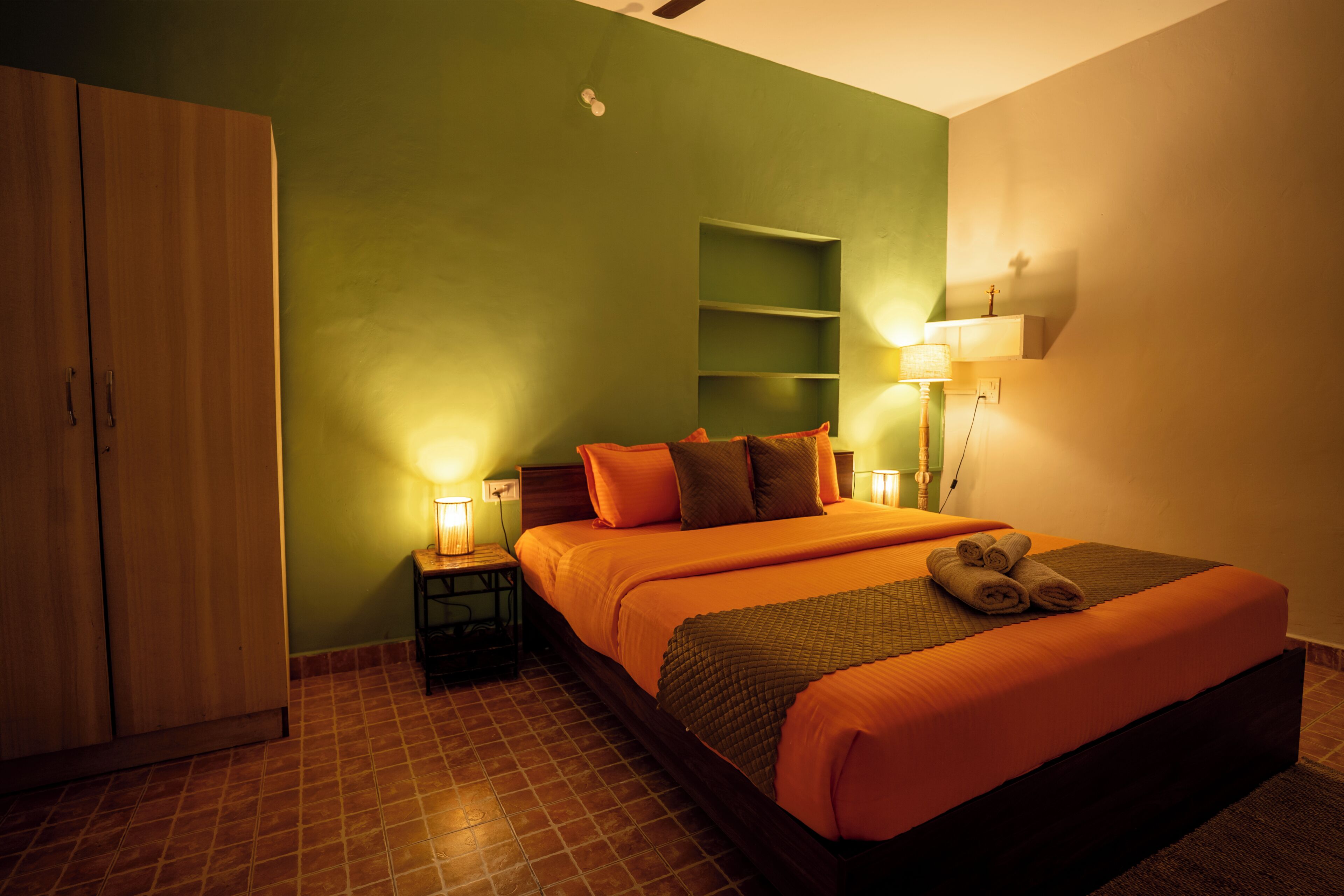 A hotel room with a bed, nightstands, a wardrobe, and a wall-mounted shelf.