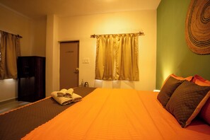 A hotel room with a bed, a door, a window with curtains, and a wall-mounted decorative item. - Seraya Stays (Mandrem)