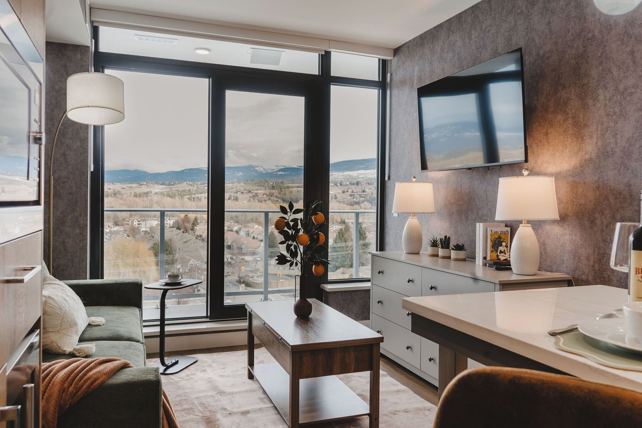 A modern living room with a sofa, coffee table, and a view of the cityscape through large windows.