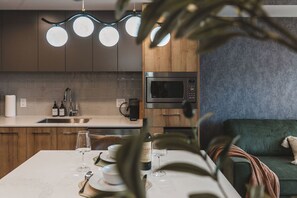 A modern kitchen with a dining area, featuring a built-in oven, a coffee machine, and a wine bottle on the table. - Luna Suite | Pet-Friendly 1BR (Kelowna)