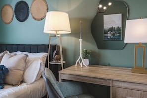 A bedroom with a bed, bedside table, lamp, wall decor, and a desk with a chair. - Luna Suite | Pet-Friendly 1BR (Kelowna)