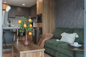A modern living room with a green sofa, a wooden coffee table, and a vase with oranges. - Luna Suite | Pet-Friendly 1BR (Kelowna)
