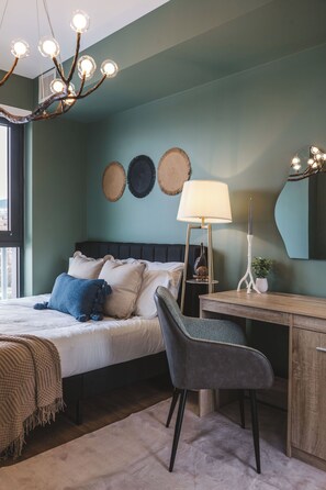 A bedroom with a bed, bedside table, lamp, chair, and wall decorations. - Luna Suite | Pet-Friendly 1BR (Kelowna)