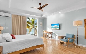 Ein Hotelzimmer mit Bett, Schreibtisch, Stuhl, Deckenventilator und Blick auf Palmen.