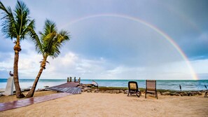 Ein Strand mit Palmen, einer Holzterrasse und Liegestühlen.