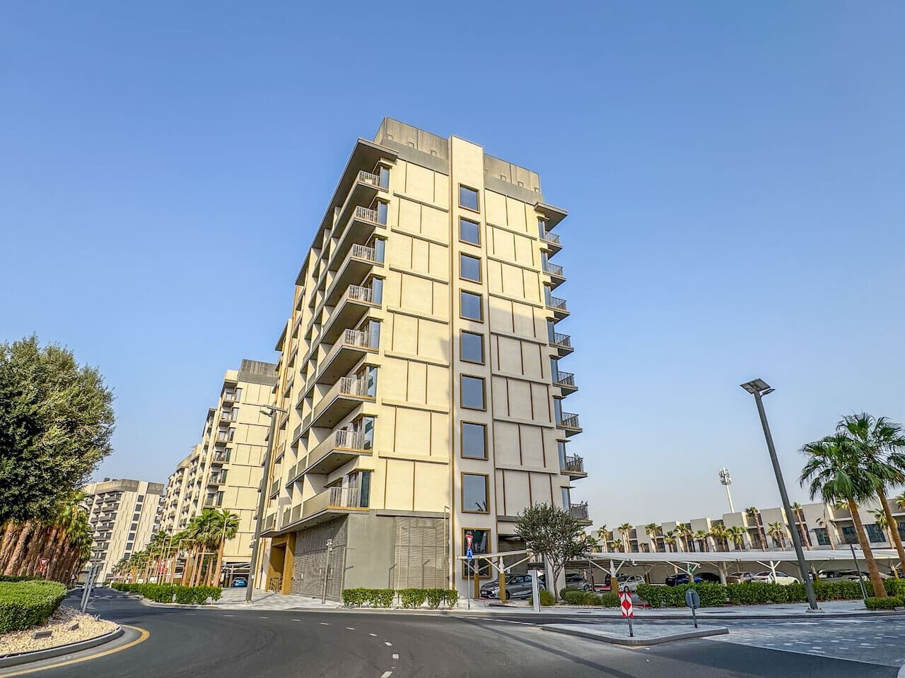 Un immeuble résidentiel à plusieurs étages, doté de balcons, d’un chemin piétonnier et surplombant un ciel dégagé.