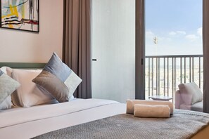 Ein Hotelzimmer mit Bett, Kissen, einem kleinen Tisch und Blick auf die Stadt durch große Fenster.