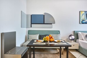 Une chambre d’hôtel moderne avec une table à manger dressée pour le petit-déjeuner, un canapé et une œuvre d’art minimaliste accrochée au mur.
