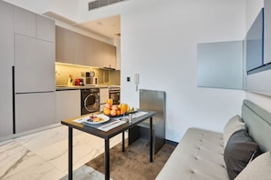 A compact living space with a kitchenette, a dining area with breakfast, and a sofa. - Stylish Modern Studio | MAG 910, Meydan Community (Dubai)