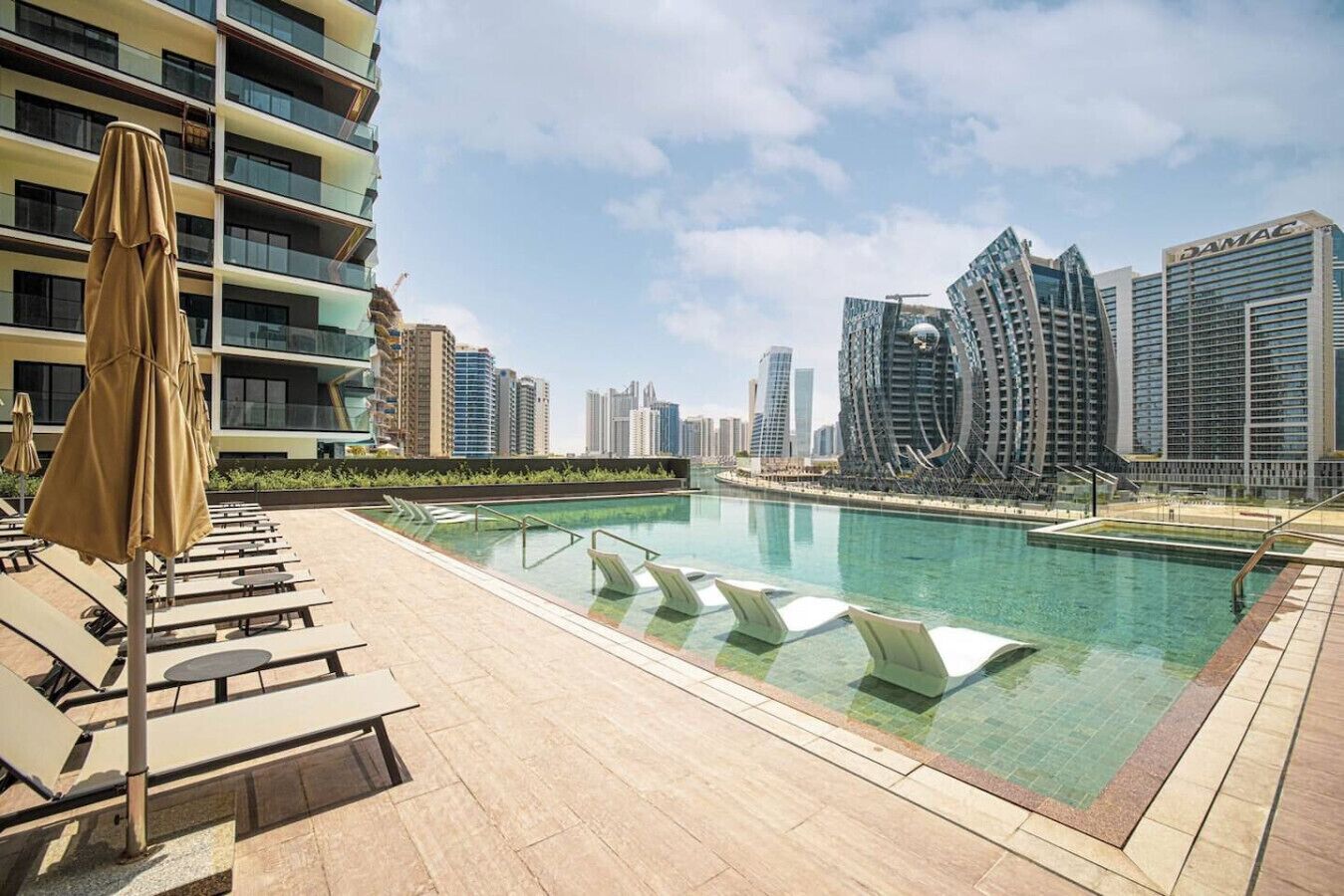 A rooftop pool area with lounge chairs and umbrellas, surrounded by high-rise buildings.