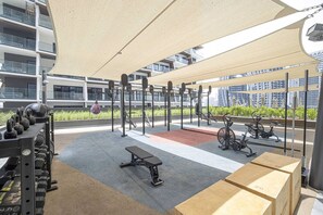 An outdoor gym with exercise equipment, a bench, and a shaded area.