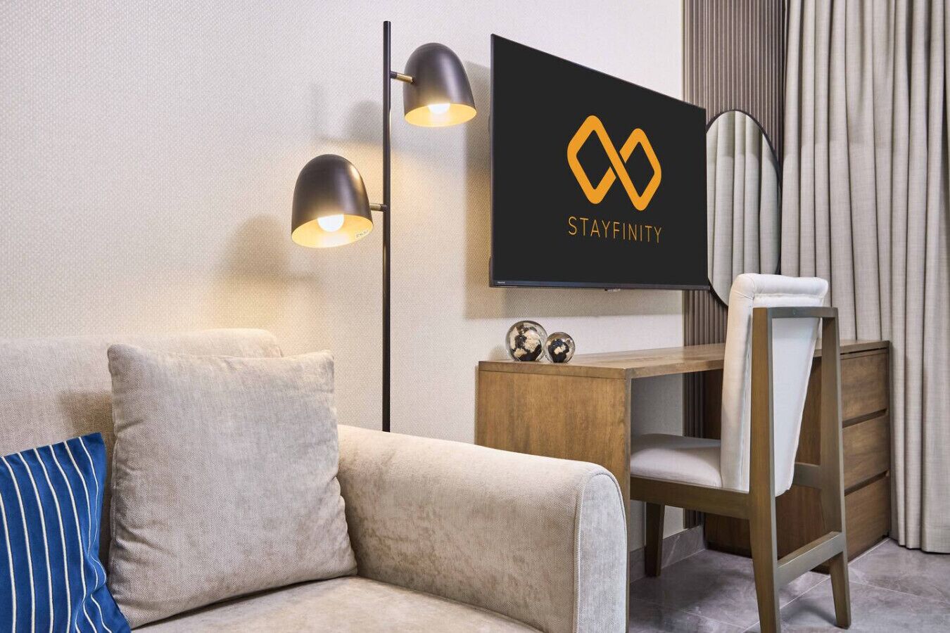 A hotel room with a sofa, a desk, a chair, a television, and a lamp.