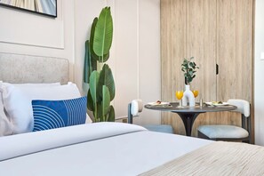 Een hotelkamer met een bed, een ronde tafel met twee stoelen, een kleine plant en een vaas met bloemen.