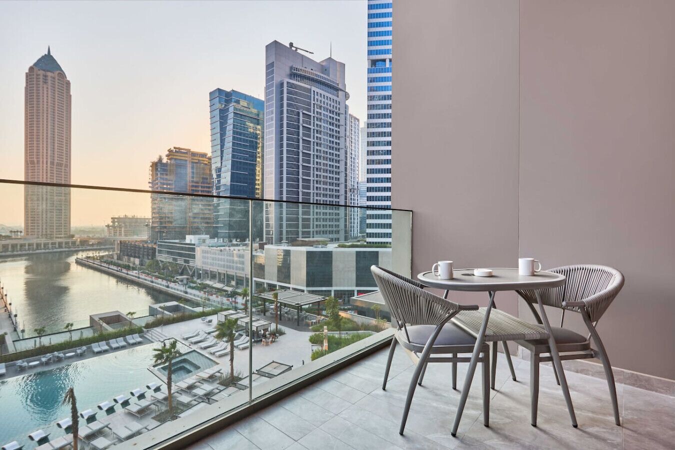 A balcony with a view of a city skyline, a pool, and a table with chairs.