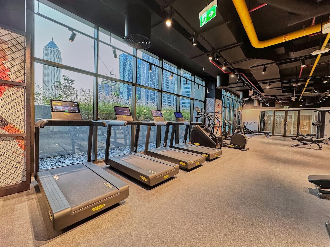 A gym with treadmills, exercise equipment, and large windows with a city view.