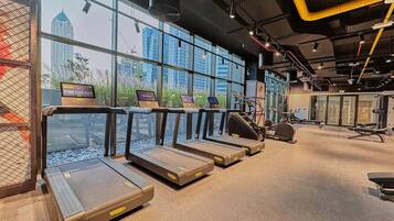 A gym with treadmills, exercise equipment, and large windows with a city view.