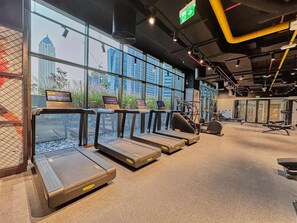 A gym with treadmills, exercise equipment, and large windows with a city view.